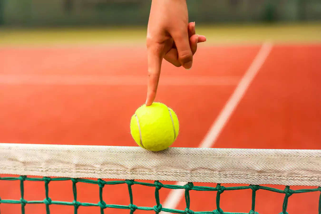 Red clay court with lady pointing at a tennis ball over the net