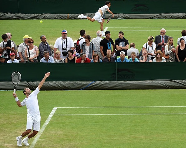 Player serving on a grass court with spectators watching the tennis match